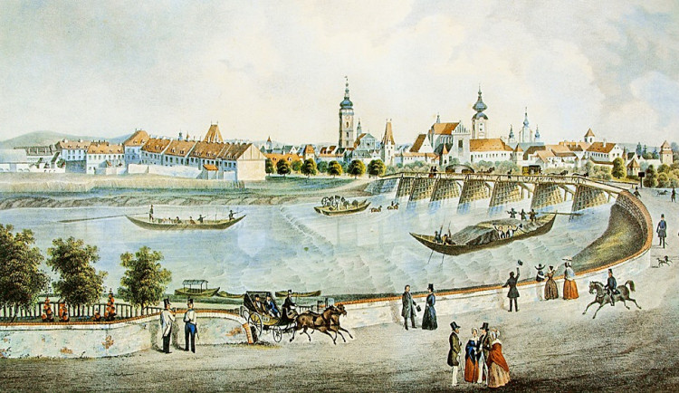 Veduta města od západu z poloviny 19. století. V popředí Vltava a lodě se starým dřevěným Dlouhým mostem. Romantické vltavské nábřeží možná tak romantické bývalo