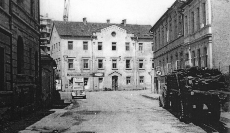 Staroměstská ulice se staroměstskou školou před rokem 1970. Zezadu se agresivně tlačí na školu panelák.