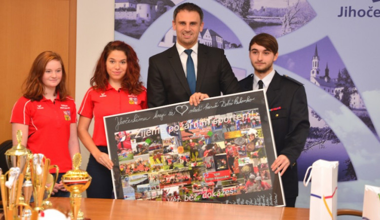 Skupinová fotka hejtmana a úspěšných mladých hasičů s koláží, kterou z fotek z požárních sportů pro hejtmana vyrobili