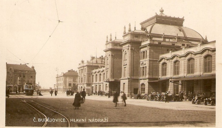 Nádražní budova s poklidným přednádražním prostorem vyhrazeným pro cestující, drožky a tramvaje