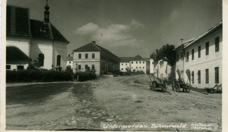 Náměstí městečka Dolní Vltavice. Mezi kostelem a školou je vidět kamenný pranýř. (Johann Mayer, nedatováno, zdroj: soukromá sbírka Jiří a Lenka Hůlkovi)