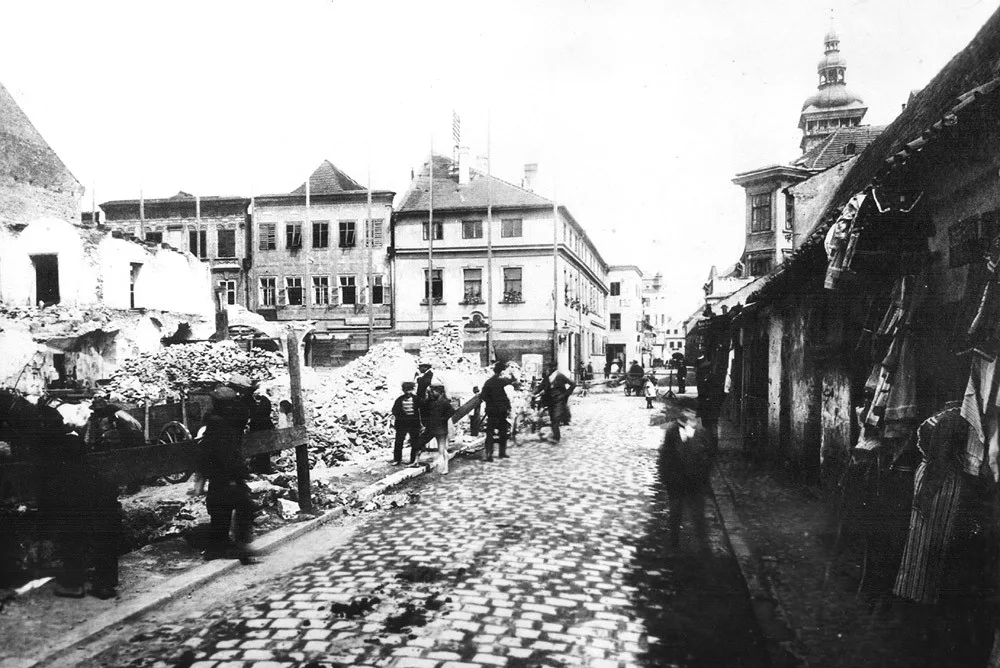 Pohled Hroznovou ulicí směrem ke Krajinské v roce 1911, kdy se bouraly domy vlevo pro stavbu německé spořitelny. Bourá se klidně, lidi si odváží materiál. Masné krámy stojí také klidně vpravo