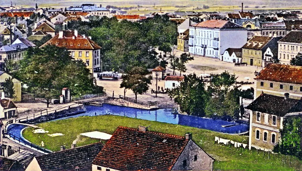 Senovážné náměstí s vodními rameny Mlýnské stoky, které vytváří ostrov, stromovím, tramvají a starou nemocnicí kolem roku 1912