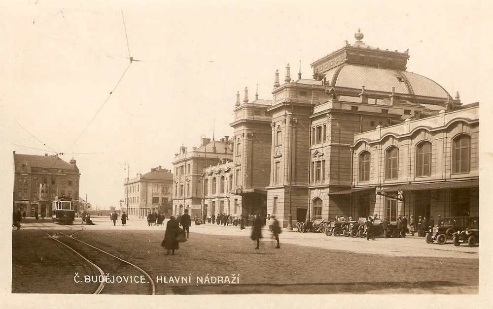 Nádražní budova s poklidným přednádražním prostorem vyhrazeným pro cestující, drožky a tramvaje