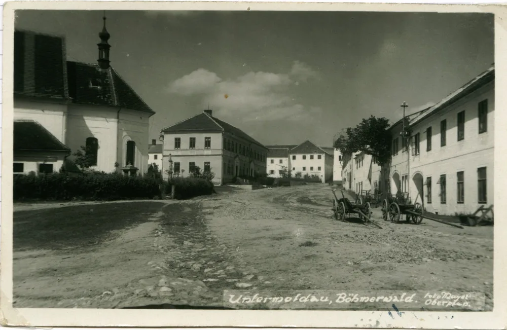 Náměstí městečka Dolní Vltavice. Mezi kostelem a školou je vidět kamenný pranýř. (Johann Mayer, nedatováno, zdroj: soukromá sbírka Jiří a Lenka Hůlkovi)