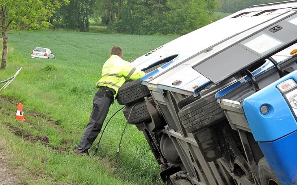 Převrácený autobus, v pozadí osobní auto, jehož řidič včas uhnul do pole
