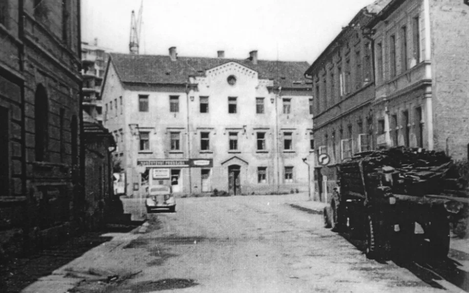 Staroměstská ulice se staroměstskou školou před rokem 1970. Zezadu se agresivně tlačí na školu panelák.