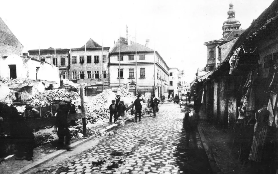 Pohled Hroznovou ulicí směrem ke Krajinské v roce 1911, kdy se bouraly domy vlevo pro stavbu německé spořitelny. Bourá se klidně, lidi si odváží materiál. Masné krámy stojí také klidně vpravo