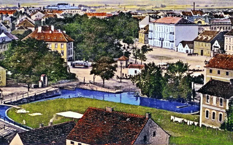 Senovážné náměstí s vodními rameny Mlýnské stoky, které vytváří ostrov, stromovím, tramvají a starou nemocnicí kolem roku 1912