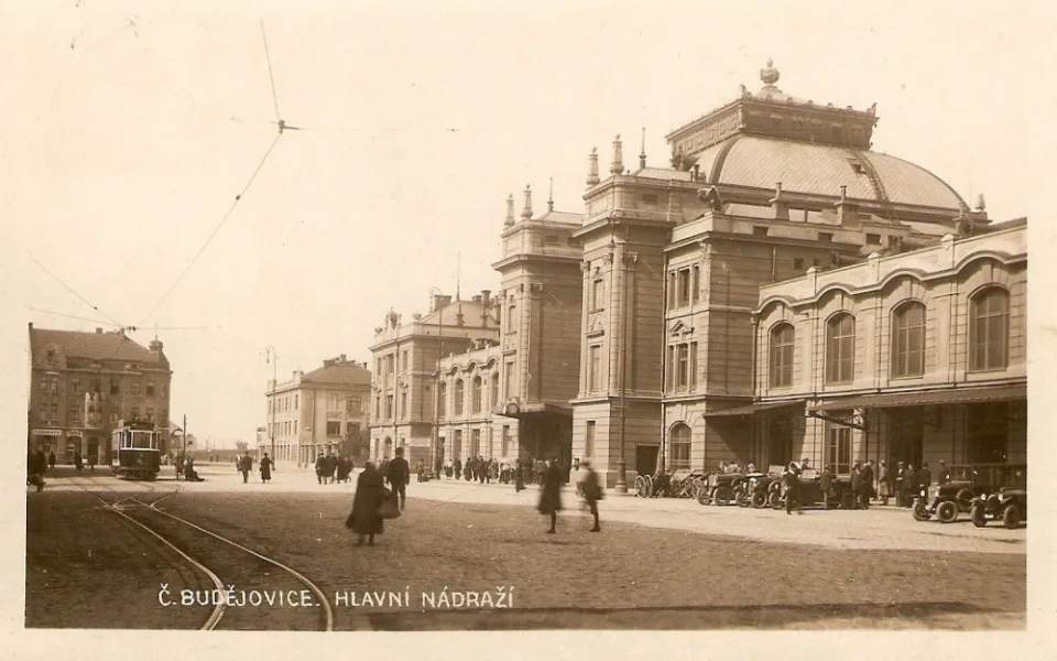 Nádražní budova s poklidným přednádražním prostorem vyhrazeným pro cestující, drožky a tramvaje